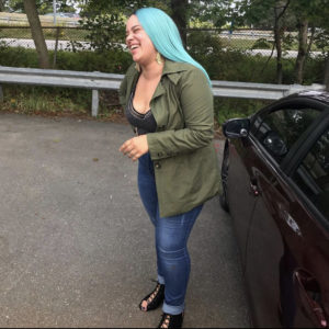 Rose bent slightly over and laughing. She is wearing a green wig, green jacket, black shirt, dark jeans, and black heels.